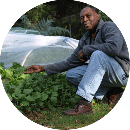 Portrait of Kenny Point crouching beside a vegetable bed